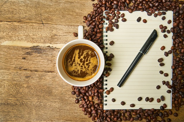 Notes s perom a šálka kávy obsypané kávovými zrnami